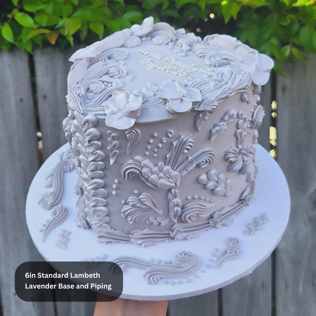 Decorative cake with intricate designs on a white stand against a wooden fence background.